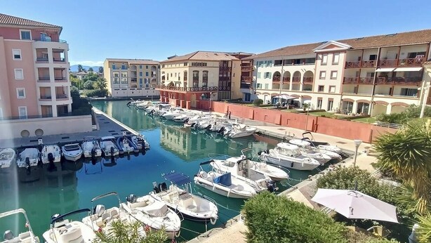 Un port esportiu amb vaixells amarrats, envoltat d'edificis de diversos pisos amb balcons.
