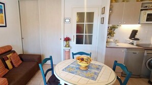 Un espai habitable compacte amb un sofà, una taula de menjador amb un plat de fruita, una zona de cuina amb microones i rentaplats, i una porta amb panells de vidre rugós.