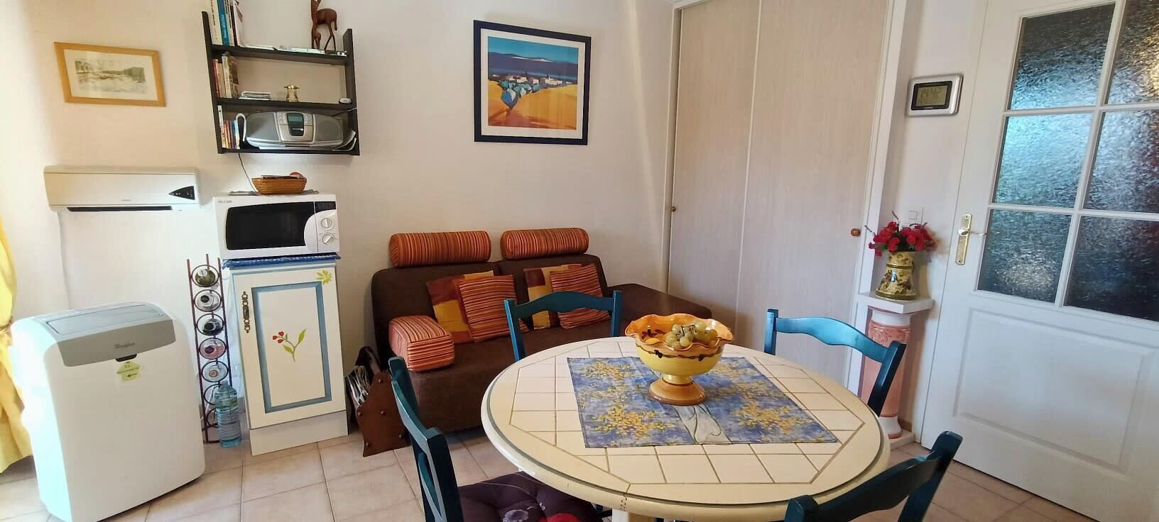 Un espacio habitable compacto con kitchenette, zona de comedor y una puerta con paneles de vidrio esmerilado.