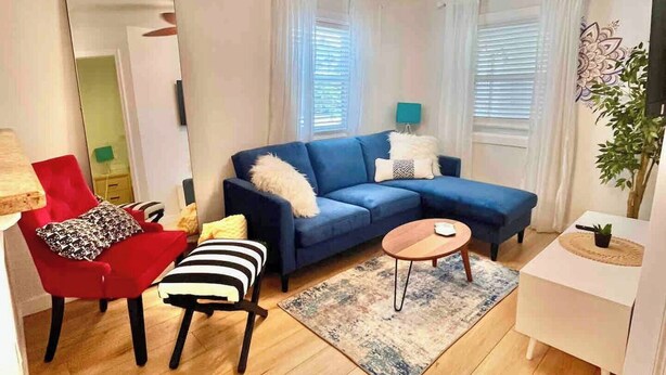 A modern living room with a blue sectional sofa, a red armchair, a striped chair, a small round table, and a ceiling fan.