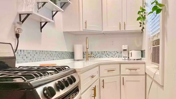 Une cuisine compacte avec des meubles blancs, une cuisinière à gaz, un four à micro-ondes et un petit plan de travail.