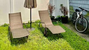 Un jardin avec deux chaises longues, un parasol et un vélo.