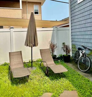 A backyard with two lounge chairs, an umbrella, and a bicycle. - Charming Coastal Retreat 1BR (Rockaway Beach)