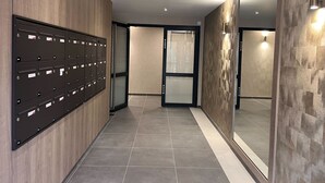 Un pasillo con una fila de buzones a la izquierda, una puerta de cristal en el centro y una pared con textura a la derecha.