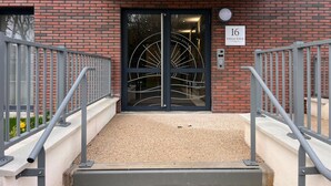 Una entrada moderna a un edificio con una puerta negra, un cartel con el número 16 y una escalera metálica que sube.