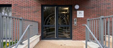A modern building entrance with a black door, a number sign '16', and a metal staircase leading up.
