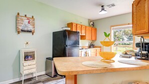 A kitchen with a refrigerator, wooden cabinets, a small white cabinet with a toy, a window with a view, and a yellow hanging basket. - Charming Ranch -Bunk North Getaway (Palm City)