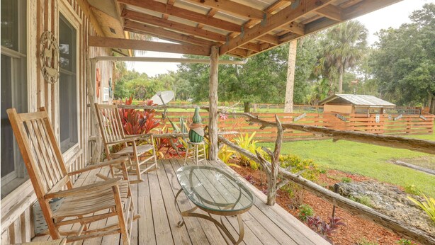 A wooden deck with chairs and a glass table, overlooking a fenced garden with various plants and a small building in the background. - Charming Ranch -Bunk North Getaway (Palm City)
