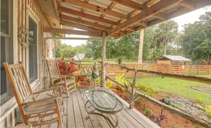 A wooden deck with chairs and a glass table, overlooking a fenced garden with various plants and a small building in the background. - Charming Ranch -Bunk North Getaway (Palm City)