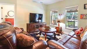 A living room with leather sofas, a wooden coffee table, a TV, and large windows with views of the outdoors. - Charming Ranch -Bunk North Getaway (Palm City)