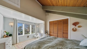 A bedroom with a large bed, a wooden wardrobe, a window with curtains, and a small table with a chair. - Boho Beach House (Tillamook)