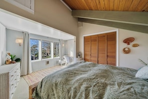 A bedroom with a large bed, a wooden wardrobe, a window with curtains, and a small table with a chair. - Boho Beach House (Tillamook)