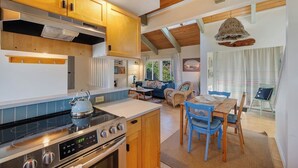 A modern kitchen with wooden cabinets, a gas stove, and a dining area with blue chairs. - Boho Beach House (Tillamook)