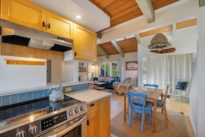 A modern kitchen with wooden cabinets, a gas stove, and a dining area with blue chairs. - Boho Beach House (Tillamook)