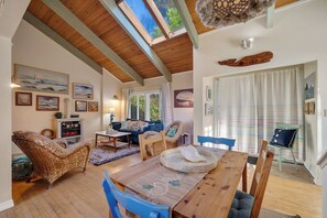 A cozy living room with a wooden ceiling, a dining table, and blue chairs. - Boho Beach House (Tillamook)