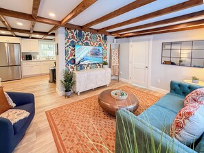 Un ampio soggiorno con una cucina moderna sullo sfondo, travi in legno al soffitto e un vivace murale.