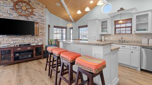 A modern kitchen with white cabinets, a wooden ceiling, and a large island with bar stools. - Stylish Canal-Front Home with Private Dock (Port Isabel)