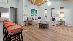 A spacious living room with a high ceiling, a sofa set, a coffee table, and a kitchen area with a refrigerator. - Stylish Canal-Front Home with Private Dock (Port Isabel)