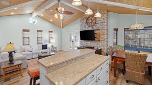 A spacious living area with a kitchen island, wooden ceiling beams, and a stone accent wall. - Stylish Canal-Front Home with Private Dock (Port Isabel)