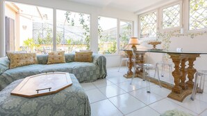 A bright room with a large bed, a dining table, and a view of the garden through large windows. - Rental in Rome Rental in Rome Tre Lune Penthouse (Rome)