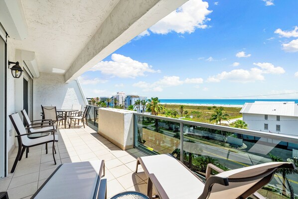 A balcony with outdoor furniture, a clear view of the beach, and a modern building in the background. - Tivoli by the Sea (Siesta Key)