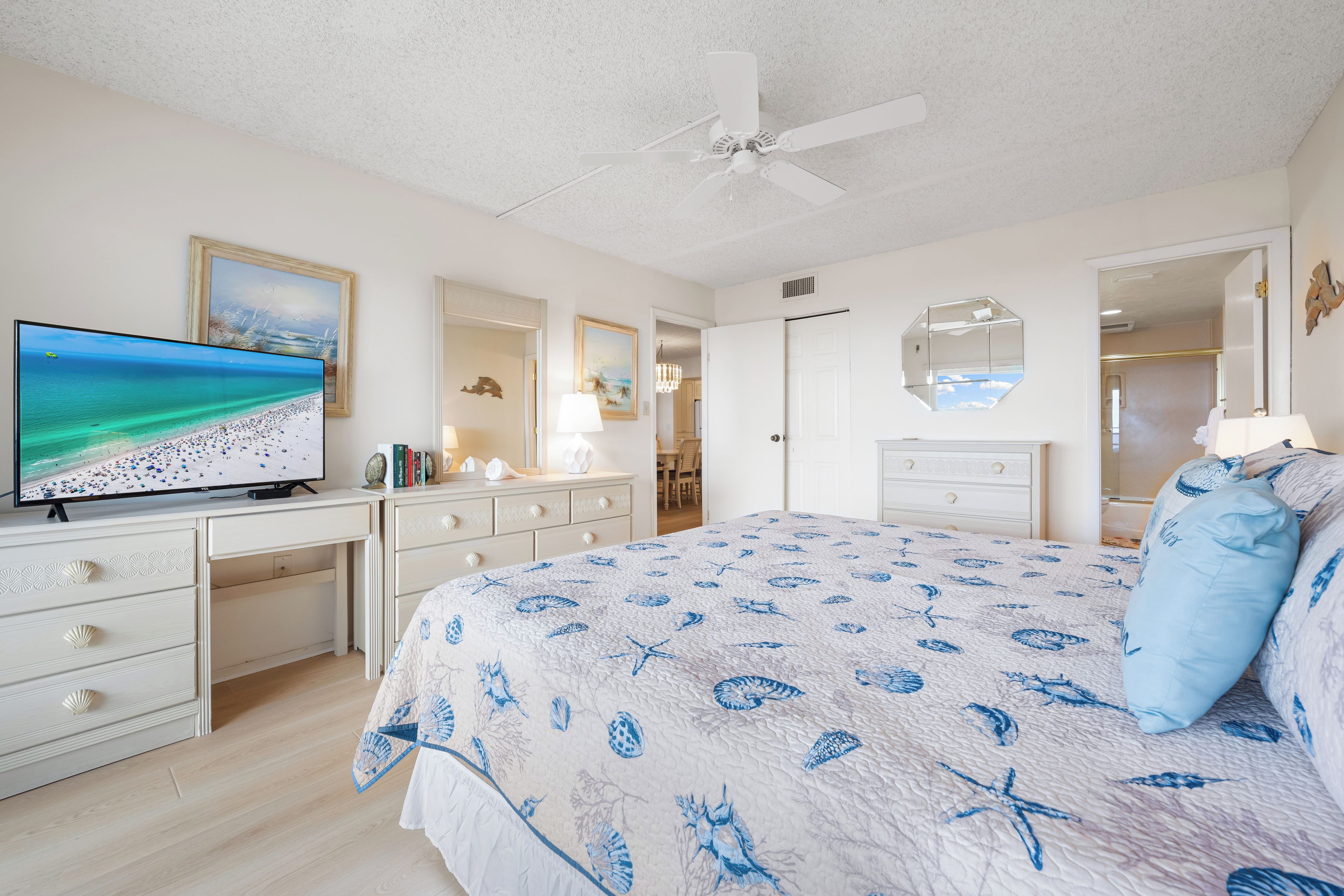 A bedroom with a bed, a TV, a desk, and a ceiling fan.