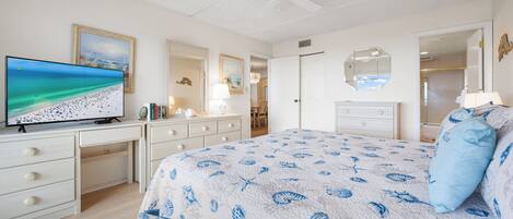 A bedroom with a bed, a TV, a desk, and a ceiling fan.