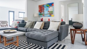 Ein modernes Wohnzimmer mit einem grauen Ecksofa, einem Couchtisch und einer Lampe auf einem Holznachttisch.