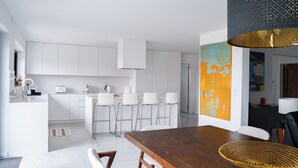 Eine moderne Küche mit weißen Schränken, einer zentralen Kochinsel mit Barhocker und einem Essbereich mit Holztisch und Stühlen.