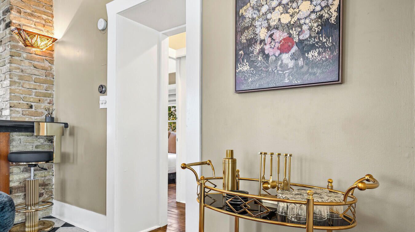 A hallway with a modern chandelier, a gold-framed side table with candles, and a floral painting on the wall.