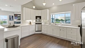 A modern kitchen with white cabinetry, a stainless steel dishwasher, and a large window offering a view of the city. - East Austin Charmer│Grill, Fenced Yard & Patio│Near Rainey, UT & 6th St (Austin)