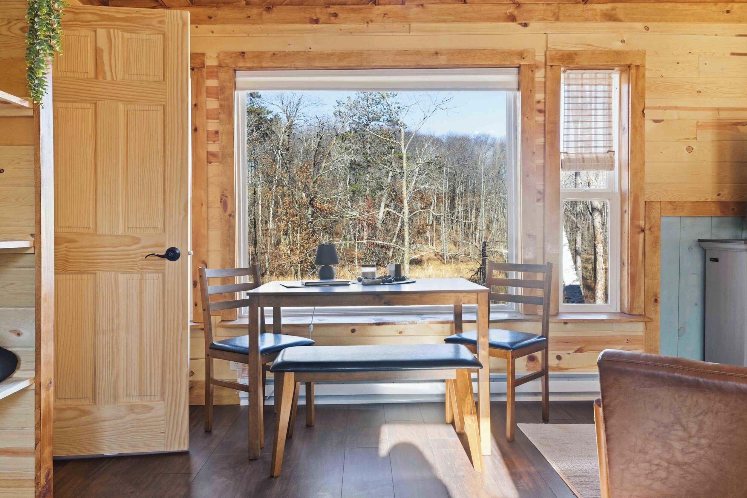 A wooden cabin interior with a dining table, chairs, and a bench.