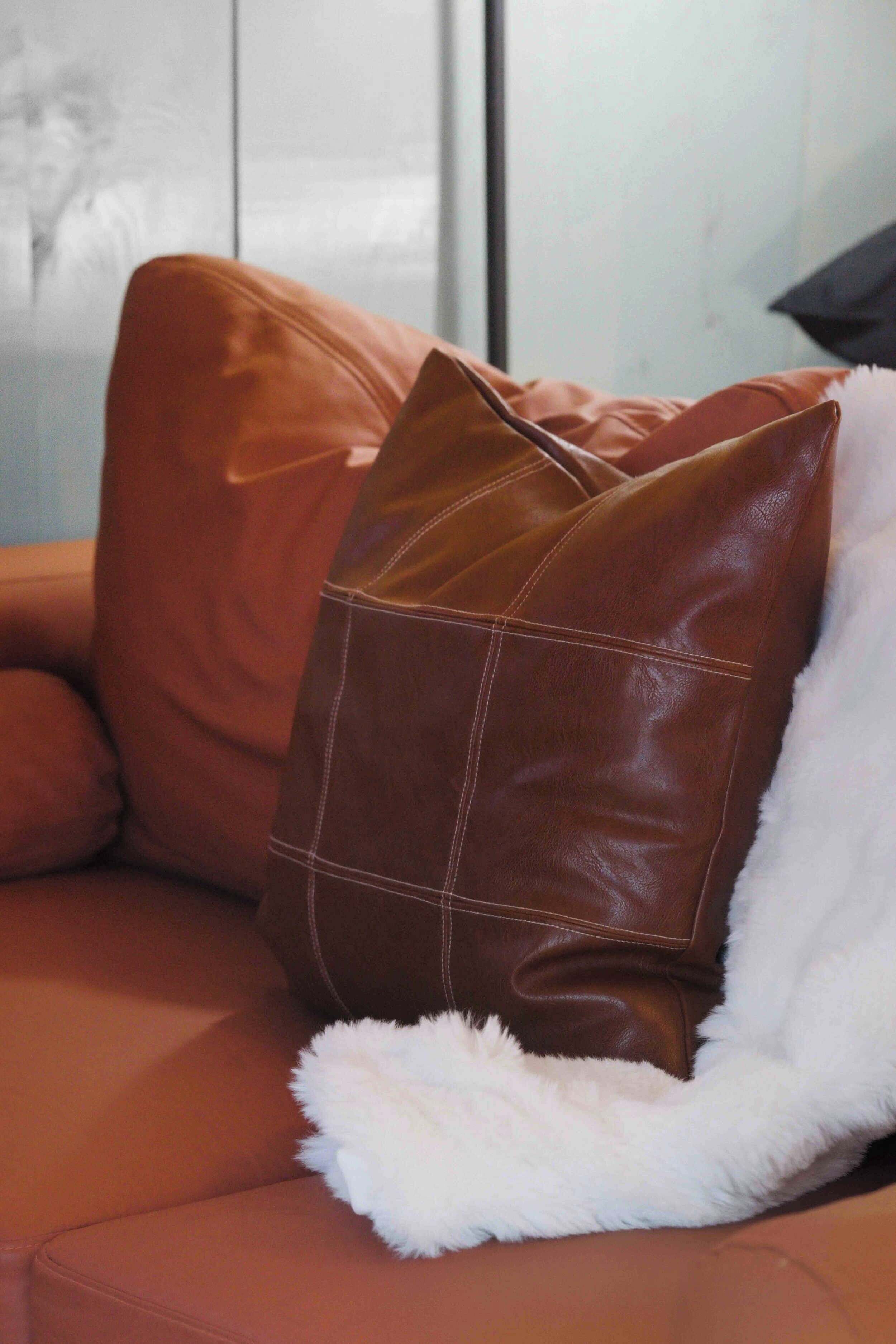 Un sac en cuir marron sur un canapé marron, avec un plaid blanc et moelleux.
