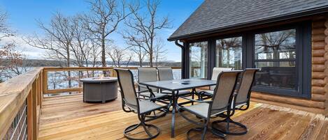 A wooden deck with a table and chairs, overlooking a body of water and trees.