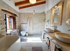 Une salle de bain moderne avec un mur en pierre, une grande baignoire, deux lavabos et une douche.