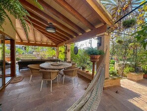 Une terrasse extérieure avec une table ronde et des chaises, un hamac et des plantes en pot.