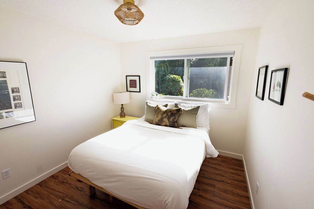 Een slaapkamer met een bed, een raam, een bedlamp en lijstjes aan de muur.