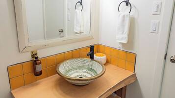 Een badkamer met een houten wastafelmeubel, een rond wastafeltje, een spiegel met gouden lijst en een handdoekrek.