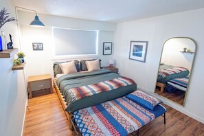 Ein Schlafzimmer mit einem Bett, einem Nachttisch, einer Lampe und einem großen Spiegel.