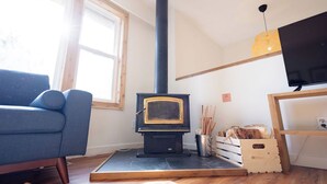 Una sala de estar acogedora con un estufa de leña negra, un sofá azul y un televisor sobre un mueble de madera.