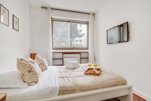 Un lit bien fait, recouvert d’une couverture moelleuse, un plateau avec des croissants et du jus d’orange, et une fenêtre donnant sur des arbres et des immeubles.