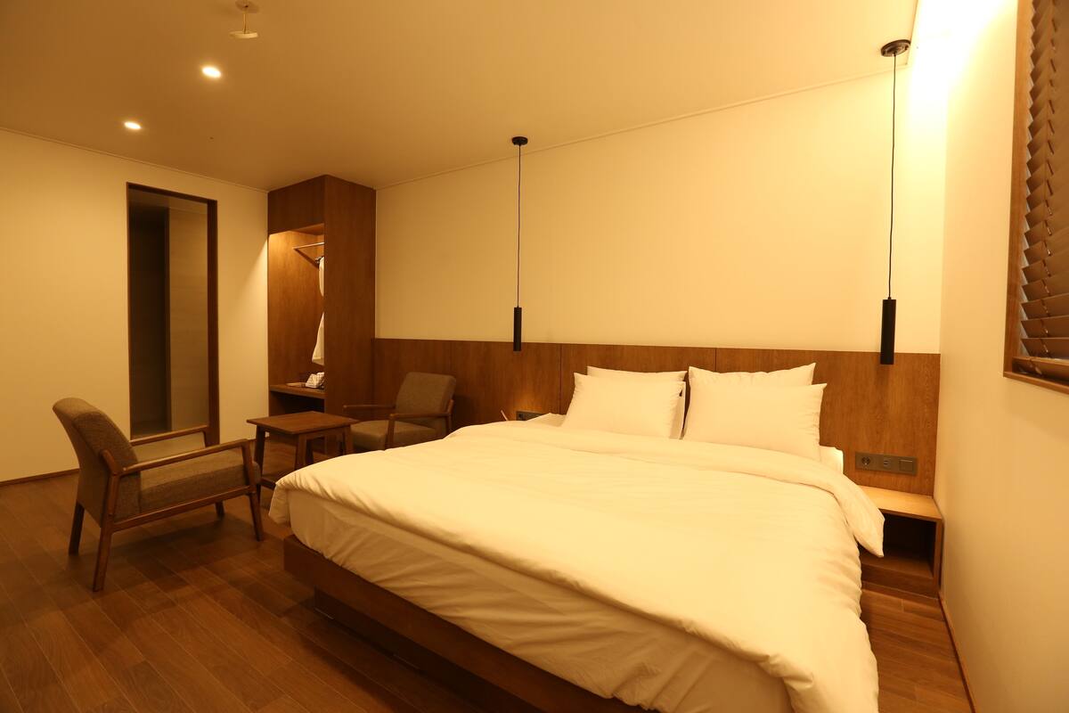Une chambre d’hôtel avec un grand lit, une chaise, une table de chevet et une tête de lit en bois.