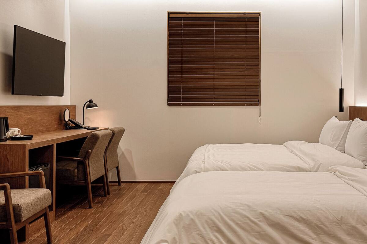 Une chambre d’hôtel avec un bureau en bois, une chaise, un lit avec du linge de maison blanc et un téléviseur fixé au mur.