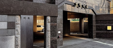 A building entrance with a sign in Korean, a parking area, and a yellow line on the pavement.
