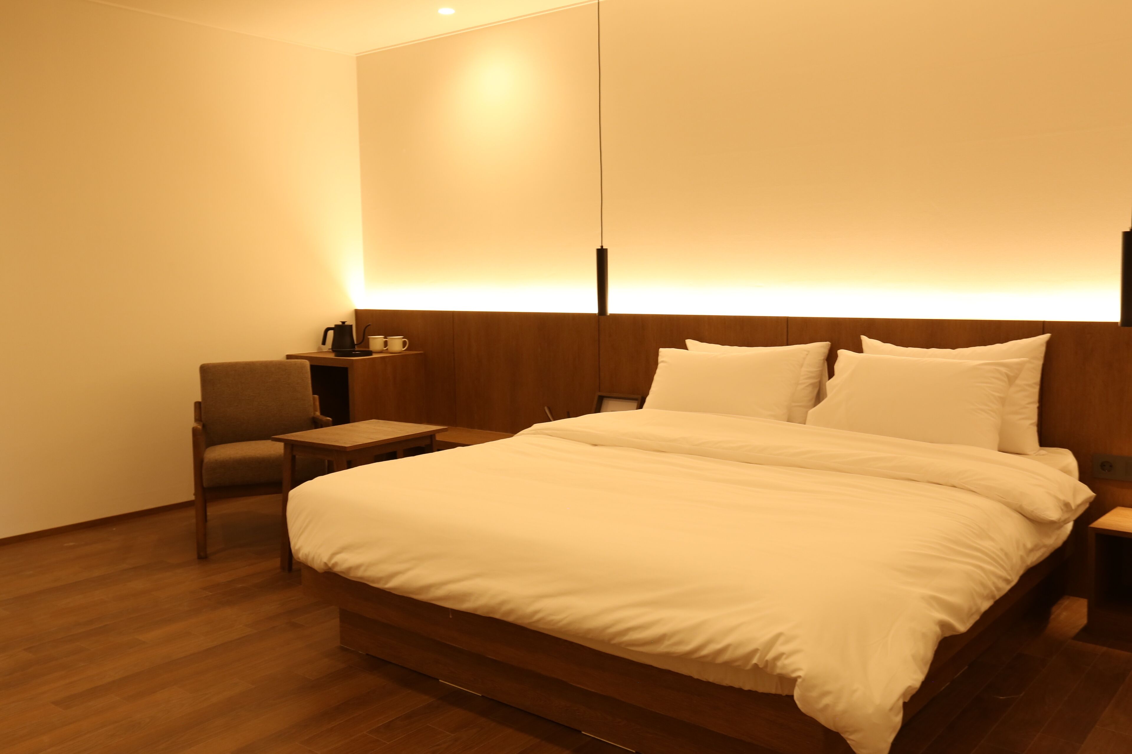 Una habitación de hotel con una cama grande, una silla, una mesita de noche y una lámpara fijada a la pared.