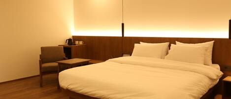 Una habitación de hotel con una cama grande, una silla, una mesita de noche y una lámpara fijada a la pared.