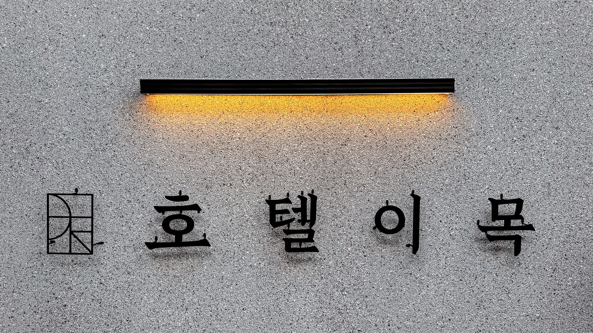 Tekstuuripintainen seinä, jossa on koreankielisiä merkkejä ja geometrinen symboli.