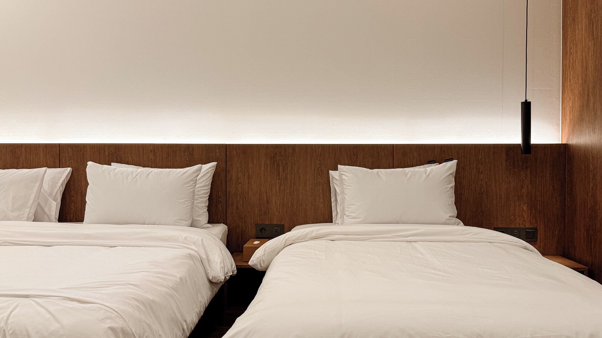 Een hotelkamer met twee bedden, een houten hoofdbord en een moderne hanglamp.