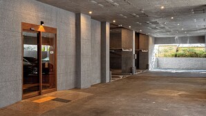 Un edificio moderno con fachada de hormigón, puerta de entrada de cristal y zona de estacionamiento visible.