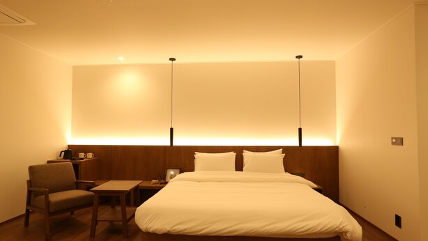 Una habitación de hotel con una cama grande, una mesita de noche de madera, una silla y una mesa.